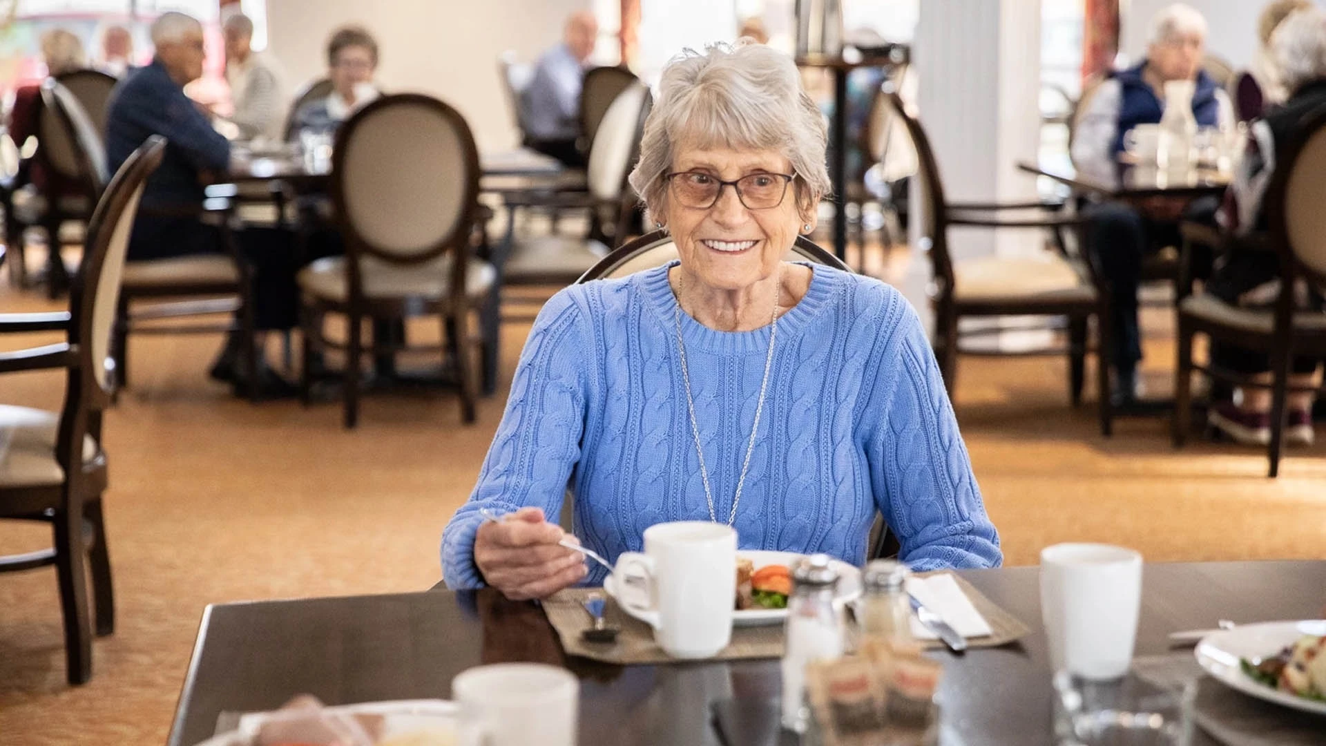 senior lady eating at a table smiling at the camera