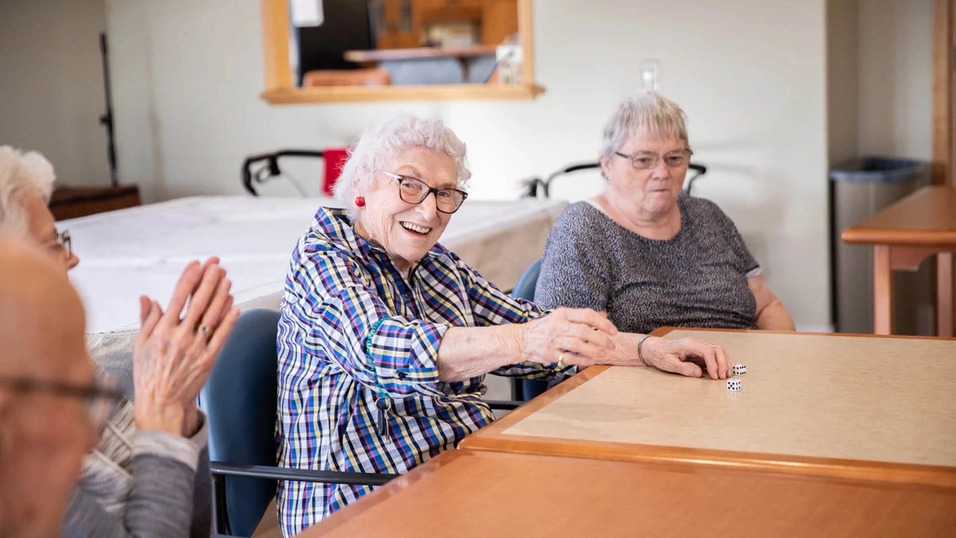 A group of elderly women clapping at a table playing with dice.