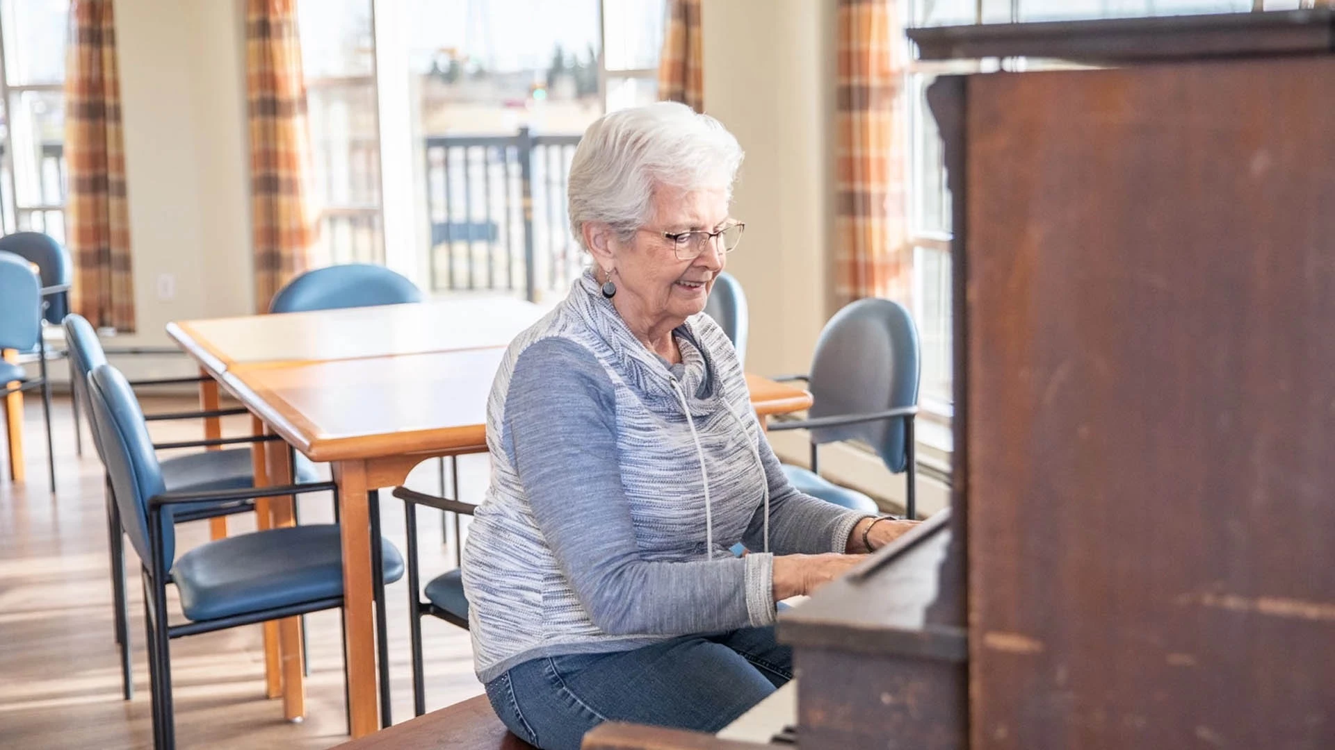 An elderly woman playing a piano in a living room.